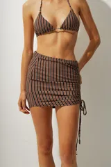 Falda corta tipo pareo con diseño de rayas verticales en tonos azul y negro. Presenta un lateral fruncido con cordón ajustable que permite regular el largo y el ajuste de la prenda.
