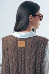 Chaleco de punto color marrón con diseño de ochos, cuello redondo y lazos laterales ajustables.