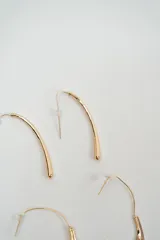 Set de tres pares de caravanas doradas de diferentes diseños: un par de aros alargados y curvos, un par de aros con dije en forma de media luna texturizada y un par de aros tipo argolla pequeña.