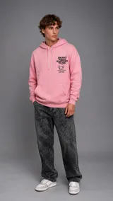 Hoodie de color rosado con capucha y cordones ajustables, bolsillo frontal tipo canguro y estampa gráfica en el pecho con texto y dibujo.