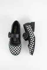 Zapato estilo Mary Jane confeccionado en cuero trenzado con diseño de damero en blanco y negro. Presenta una tira con hebilla circular en el empeine y un taco bajo cuadrado.