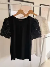 Remera blanca de algodón con mangas cortas abullonadas decoradas con apliques de flores en relieve. Presenta cuello redondo y un diseño versátil ideal para diversas ocasiones.