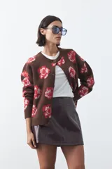 Cardigan de tejido jacquard color marrón con estampado floral en tonos rojo y rosado. Presenta cuello redondo, cierre frontal con botones y terminaciones acanaladas en puños y ruedo.