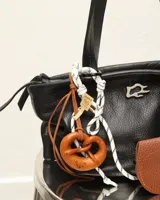 Llavero con dije de pretzel marrón, cordón blanco y negro, y detalles en cuero. Incluye mosquetón metálico para colgar en carteras o bolsos.