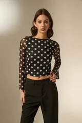 Top de manga larga confeccionado en tejido de tul semitransparente con estampado de lunares blancos sobre fondo negro. Presenta un corte ajustado al cuerpo, cuello a la base y mangas acampanadas.