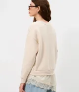 Buzo de algodón con felpa, corte oversized, cuello redondo y mangas largas. Presenta un detalle de encaje aplicado en el ruedo, aportando un contraste femenino y sofisticado.