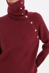 Sweater de punto en color bordó, con cuello alto tipo polera y cierre lateral mediante botones dorados. Presenta mangas largas y un diseño de tejido acanalado.