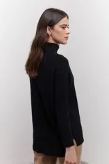 Polera de tejido de punto acanalado en color negro, con cuello alto y diseño de corte recto con largo asimétrico, más corto adelante y más largo atrás.