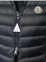 Chaleco puffer Moncler modelo Igens, de color negro con diseño acolchado horizontal, cierre frontal con cremallera y bolsillos laterales. Presenta cuello alto y el parche con el logotipo de la marca en el pecho.