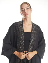 Ruana de tejido soft color negro, con detalles de brillos y tachas en los bordes frontales. Presenta una caída fluida y terminación con flecos.