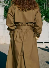 Trench coat de algodón en color verde oliva, con diseño largo y oversize. Presenta cuello camisero de pana, cierre de doble botonadura, cinturón con hebilla, trabillas en hombros y puños ajustables.