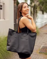 Bolso tipo tote de cuero negro, hecho a mano, con detalle de costura decorativa en el borde superior y asas largas para llevar al hombro.