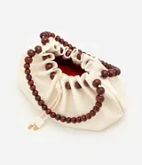 Cartera hobo marca Satinato en poliuretano color marfil, con diseño fruncido, cierre de cordón ajustable y asa rígida de esferas de madera.
