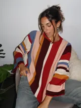 Sweater tejido a mano con terminaciones en crochet, de silueta oversize y mangas acampanadas. Presenta un diseño de rayas verticales multicolores en tonos tierra, rojo, azul y crema.