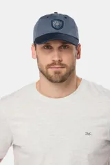Gorro tipo gorra con visera de lona color azul, con parche tejido frontal que presenta diseño de paisaje y mar.