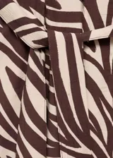 Vestido midi de corte recto con estampado animal print tipo cebra en tonos marrón y beige. Presenta cuello camisero, cierre frontal con botones, mangas cortas con vuelta y cinturón tipo batín para ajustar a la cintura.
