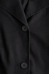 Chaqueta negra de corte relajado confeccionada en mezcla de algodón y lyocell, con solapas anchas redondeadas, hombros caídos, botonadura frontal y bolsillos delanteros de parche.