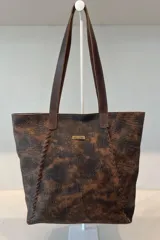 Bolso grande tipo tote color beige con textura tejida y costuras decorativas en los laterales. Tiene doble asa de hombro y logo de la marca en el frente. Interior forrado con bolsillo con cierre y portacelular.