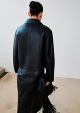 Chaqueta de cuero sintético color negro, con cuello camisero, cierre frontal oculto y mangas largas con puños rectos.