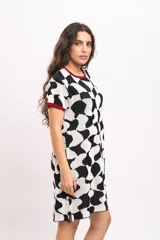 Vestido corto de tejido de punto con diseño abstracto en blanco y negro, mangas cortas y detalles en color rojo en el cuello y los puños.