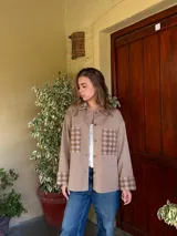 Camisa tejida de lana en color beige, con diseño de corte recto y holgado. Presenta bolsillos frontales y puños con estampado de cuadros en tonos marrones, cierre frontal con botones y cuello clásico.
