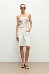 Top blanco de tirantes finos con detalle de encaje en escote y dobladillo, con bordado floral multicolor en el frente.