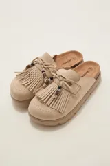 Suecos tipo mule de gamuza color beige, con detalle de flecos frontales, lazo decorativo y cuentas de madera. Poseen suela de goma con plataforma.