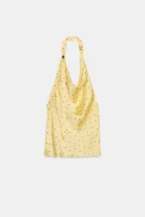 Top amarillo con lunares negros, cuello halter y escote fluido. Tiene un aplique metálico en el cuello y la espalda descubierta.