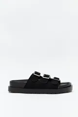 Sandalia negra tipo slide con plataforma gruesa y tres tiras ajustables con hebillas metálicas plateadas. La capellada es de material con textura de gamuza o nobuck.