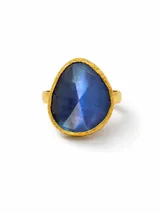 Anillo con piedra de cuarzo azul facetada en forma de gota, montada sobre una base de bronce con acabado dorado y borde texturizado.