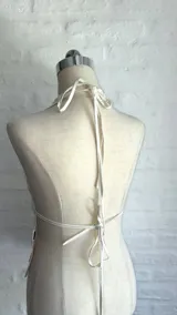 Top halter color beige claro, ajustado al cuerpo, con escote pronunciado en V y cubierto de lentejuelas redondas. Se ajusta mediante tiras en el cuello y la espalda.