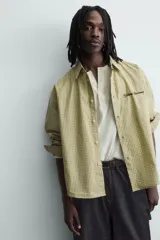 Camisa de corte boxy fit confeccionada en tejido de algodón con estampado de cuadros. Presenta cuello solapa, manga larga con puños abotonados, bolsillo plastrón en el pecho y cierre frontal de botones. Incluye un bordado a contraste en el pecho.