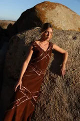 Vestido midi de gamuza color marrón cognac, con escote en V y detalles de calados geométricos artesanales en rombos. Presenta costuras decorativas con ribetes de cuero metalizado en tono cobre.