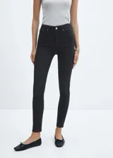 Jeans skinny de tiro alto en color negro, con diseño de cinco bolsillos, trabillas para cinturón y cierre frontal con cremallera y botón.