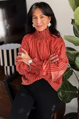 Blusa de tela liviana con diseño de rayas verticales en color terracota y blanco. Presenta cuello alto con detalle de smock, mangas largas con volumen y puños también con detalle de smock.