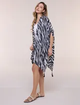 Kimono confeccionado en gasa ligera de poliéster, con diseño estampado animal print de cebra en color blanco y negro. Presenta silueta amplia, mangas cortas integradas y ruedo asimétrico con detalles de borlas en las puntas.