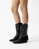 Bota de cuero negro estilo texano, con taco bajo y punta fina. Incluye un aplique desmontable en la zona del empeine decorado con tachas metálicas y flecos largos.