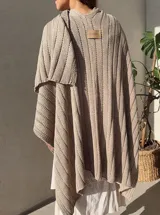 Ruana tejida en punto jersey, color negro con destellos brillantes de lurex. Presenta una etiqueta de cuero sintético con logo en la parte posterior.