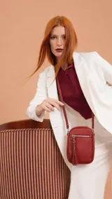 Bandolera compacta tipo porta celular color rojo, con correa regulable y desmontable. Presenta un bolsillo frontal con cierre y detalle de borla decorativa, y cierre principal superior.