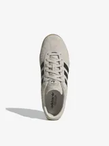 Zapatillas Adidas Gazelle Lo Pro color gris claro con las tres tiras laterales en negro y suela de goma color caramelo.