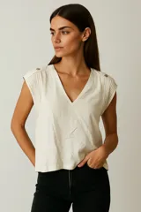 Blusa color crema de viscosa con cuello en V y detalle de pliegues en los hombros con botones decorativos.