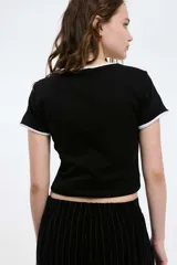 Remera baby blanca de algodón, de corte cropped al cuerpo y mangas cortas. Presenta ribetes negros en contraste en el cuello redondo y los puños, con un estampado localizado de un ají rojo con la inscripción 'Pimentón' en el centro del pecho.