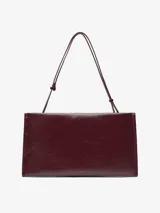 Bolso tipo clutch de Adolfo Dominguez en color bordó con acabado brillante y textura craquelada. Cuenta con un compartimento principal con cierre magnético, bolsillo interior con cremallera, asa de mano integrada y asa larga regulable y extraíble.