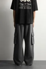 Pantalón jogger de corte relajado confeccionado en tejido de algodón compacto con elasticidad. Presenta cintura elástica ajustable con cordón, bolsillos laterales, bolsillos cargo con solapa en las piernas y detalle de pliegues en las rodillas.