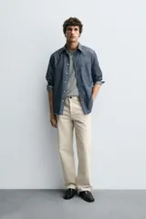 Pantalón chino de algodón color beige claro, corte recto, con cierre frontal de cremallera y botón, bolsillos delanteros y bolsillos traseros de doble vivo con botón.