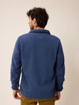 Campera de polar color beige con cierre frontal completo y cuello alto. Presenta un bolsillo en el pecho con cierre y detalle de parche con logo. El diseño combina paneles de tejido polar con detalles en tejido técnico en la zona del pecho.