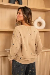 Sweater gris de corte holgado con cuello redondo y mangas largas. Presenta detalles de ojales metálicos dorados y plateados en el frente y las mangas.