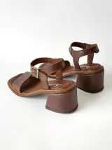 Sandalias de cuero color chocolate, con taco cuadrado de 6 cm, tira ancha en la parte delantera y tira en el tobillo con hebilla metálica ajustable.