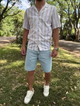 Camisa de manga corta con estampado de rayas verticales en tonos beige y blanco, cuello abierto tipo cubano y cierre frontal con botones marrones.