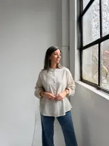 Camisa beige de lino de corte holgado, con cuello mao, mangas largas con puños fruncidos y cierre frontal de botones.